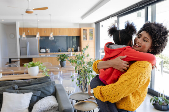 Hugging African American mother and daughter in open-plan kitchen, with pendant lights, copy space