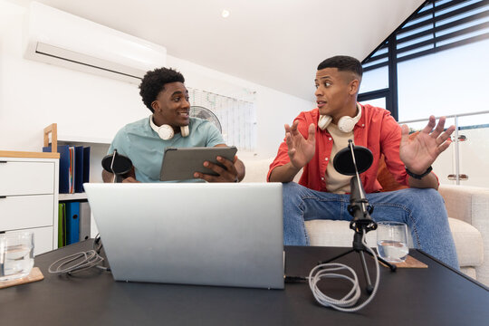 Diverse male colleagues recording podcast in home studio, with laptop, microphone and headphones