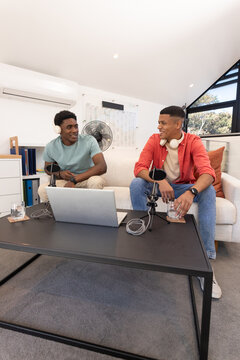 Recording Diverse coworkers conversing on podcast in living room loft with microphones and laptop