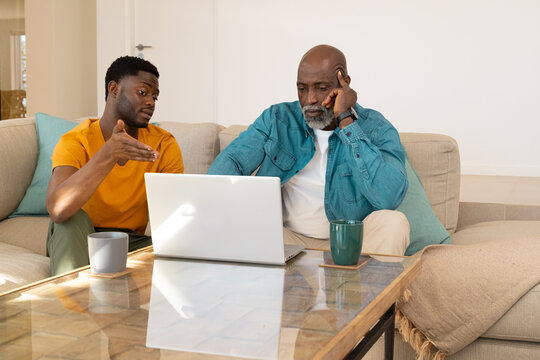 Talking African American father and son reviewing laptop at home, with mugs and teal pillows