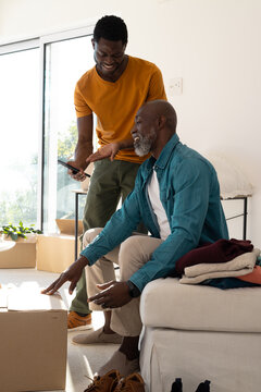 Unpacking African American father and son sorting clothes on couch in living room, with smartphone