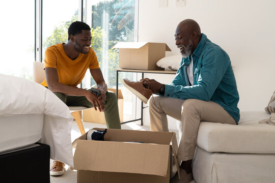 Unpacking African American father and son beside moving box at home, holding sneaker and smartphone