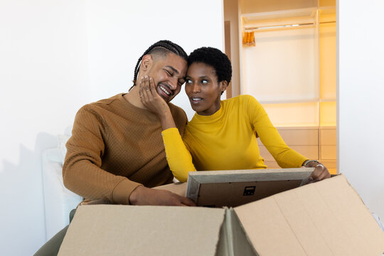 Unpacking Diverse couple sorting belongings on couch in living room, with box and framed picture