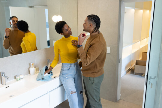 Diverse couple shaving together at bathroom sink vanity, with electric razor and toiletry items