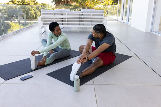 African American friends performing hamstring stretch on rooftop with yoga mats and water bottle