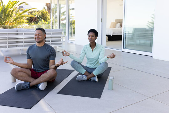 Meditating diverse friends holding hands on tiled patio, with two black yoga mats and water bottles