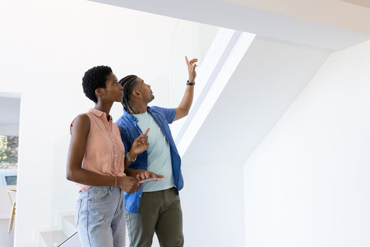 Looking upward at skylight in modern home, Diverse couple holding tablet with smartwatch