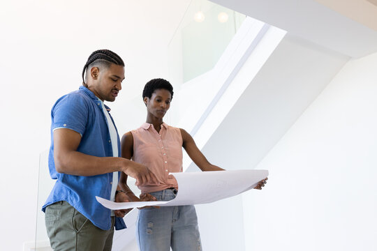 Examining Diverse coworkers collaborating on blueprint in modern interior, with glass staircase