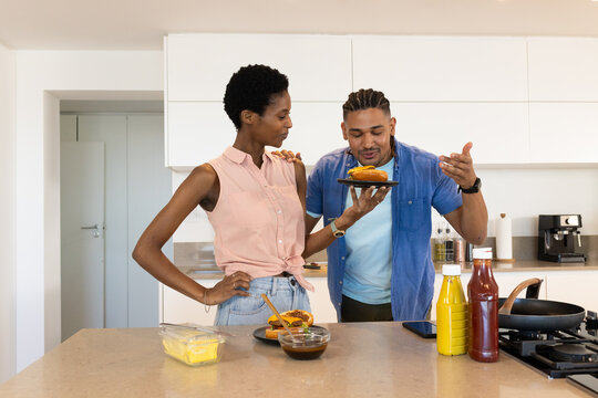 Cooking couple preparing burgers at kitchen island, tasting sauce with spatula and margarine tub