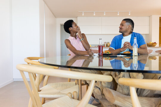 Talking Diverse friends sitting at glass-top dining table in kitchen, with sandwiches and drinks