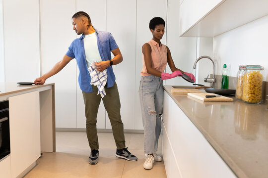 Diverse couple washing dishes in modern home kitchen, with frying pan and soap bottle