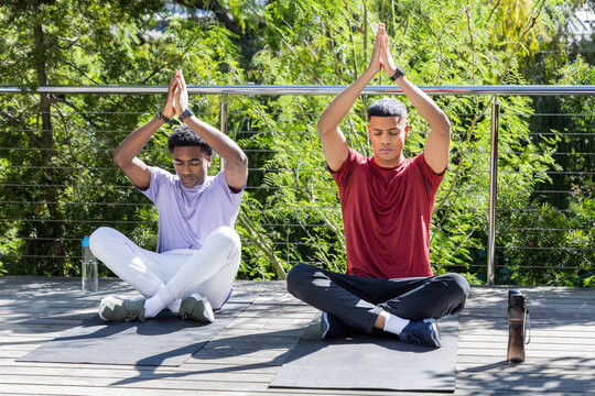 Practicing Diverse male friends pressing hands overhead on deck, with yoga mats and water bottles