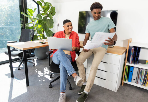 Collaborating male colleagues reviewing documents in modern office, using laptop and binders