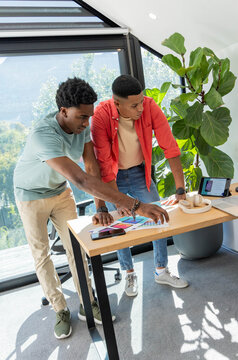 Diverse male coworkers leaning over desk examining color palette samples and smartphone in studio