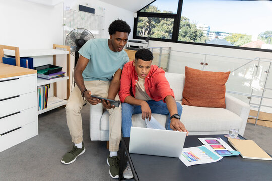 Collaborating diverse male coworkers using laptop and tablet in office lounge, with color swatches