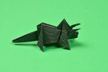 A dark green origami triceratops with light green stripes stands on a solid bright green surface © nahhan