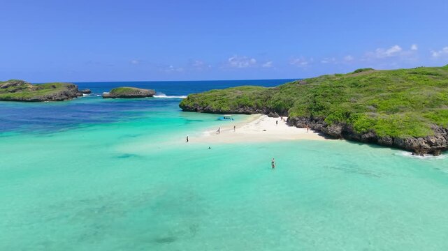 Aerial view of people swimming and walking on a white sandbar surrounded by turquoise water and green rocky islands at Watamu Beach, Kenya.