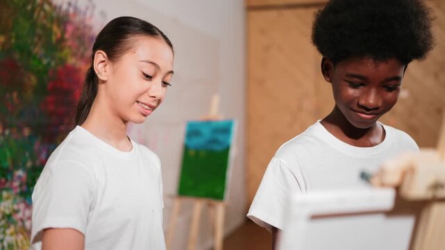 Diverse children in casual shirt painting canvas together in creative art lesson. Multicultural happy high school student drawing a same canvas while standing at colorful stained wall. Edification