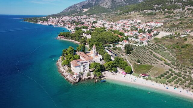 Aerial view of the monastery nestled on a small rocky promontory surrounded by a white sandy beach, the turquoise waters contrast with the rocky shore, Bol, Dalmatian Coast, Croatia.