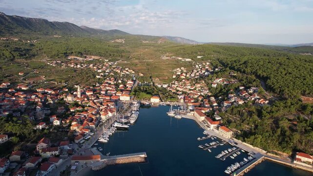 Aerial view of the vibrant Jelsa town, where terracotta roofs meet the azure harbour, framed by verdant hills, Jelsa, Split-Dalmatia County, Croatia.