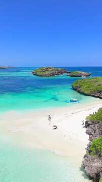 Aerial view of rocky islands and a white sand beach with a woman and a child near turquoise water at Watamu Beach, Kenya.