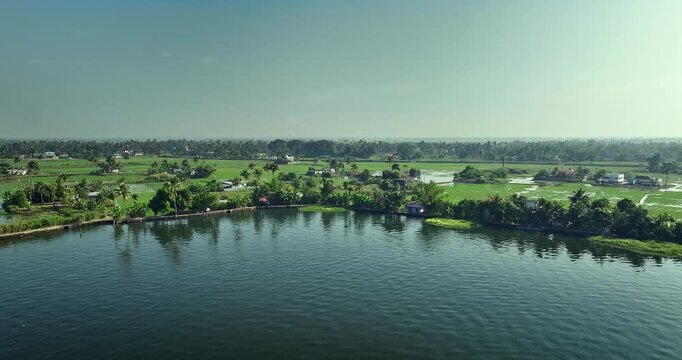 Aerial view of the Alleppey backwaters in Kerala showing traditional boats, narrow canals, palm-lined banks, village houses, and lush green paddy fields, famous tourism destination in South India.