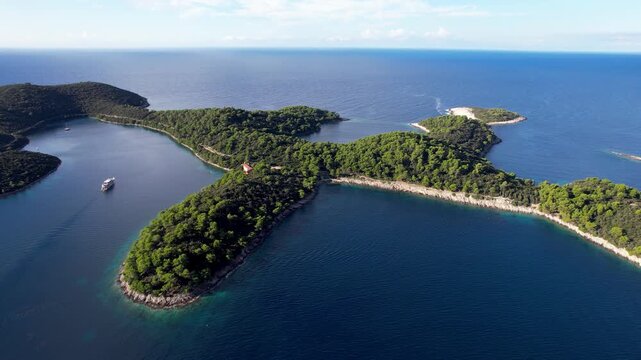 Aerial view of the vivid green Mljet National Park islands surrounded by the deep blue Adriatic sea and a boat sailing near Pomena, Dubrovnik-Neretva County, Dalmatian Coast, Croatia.