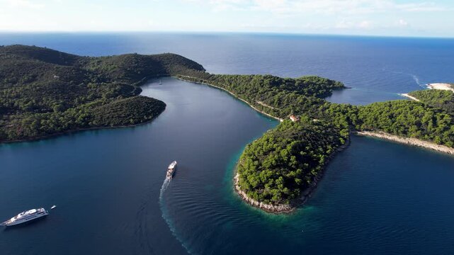 Aerial view of boats sailing through the dark blue waters surrounding the lush green Mljet National Park, Pomena, Dubrovnik-Neretva County, Dalmatian Coast, Croatia.