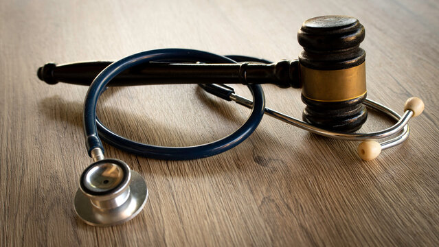 Medical stethoscope and a wooden judge gavel resting together on a wooden desk