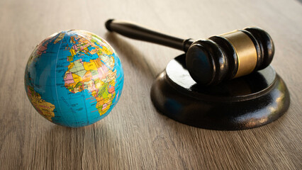 A wooden judge gavel sitting on a sound block next to a colorful world globe on a desk.