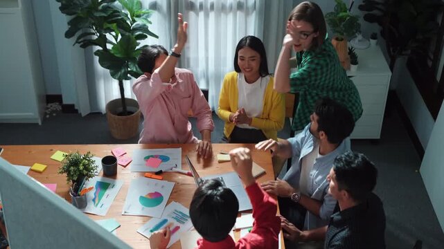 Top view of creative team giving high five to celebrate increasing sales or successful idea. Group of diverse people brainstorming marketing plan by using sticky note while clapping hands.Convocation.