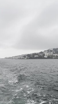 White boat navigating the gray water near Istanbul's Kinaliada Prince Island. Authentic, unfiltered vertical footage on a misty overcast day with a view of the distant city shoreline.