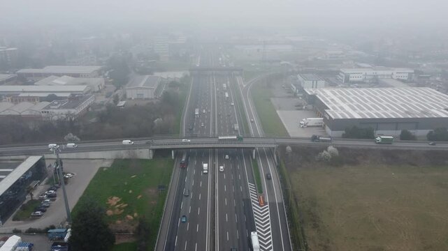Aerial view of A4 freeway in Cavenago di Brianza near Milano, Lombardia, Italy with smog, pollution, fog. Italian landscape with industrial buildings and highway travel