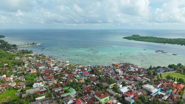 Aerial view of boats scattered across the turquoise waters near a coastal village, contrasting with the lush green island, Karimunjawa, Central Java, Indonesia.