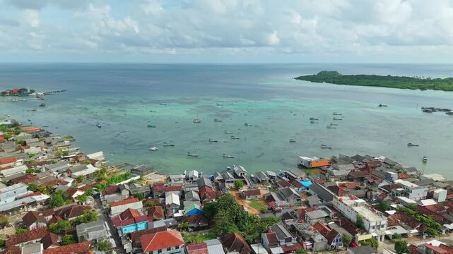 Aerial view of the Karimunjawa coastline with its colorful houses, boats, and a lush island against the backdrop of the turquoise ocean, Karimunjawa, Central Java, Indonesia.