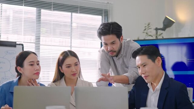 Professional Asian business team meeing discussing project updates and collaborating on laptop during a routine office meeting.