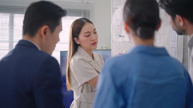 Asian business woman and team discussing application workflow, data analysis, and team tasks pinned on a whiteboard during a strategic meeting.