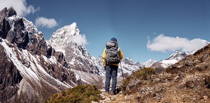 Hiker backpacker admiring Panoramic View of Snowy Himalayan Range on trail during sunny day on his trek to Everest Base Camp in Nepal.