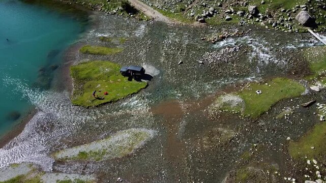 Aerial high angle of an off-road SUV at a river delta by a turquoise lake; a metaphor for reaching the goal and remote basecamp