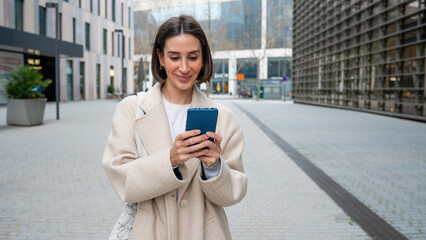 Woman smiling and using phone in urban setting