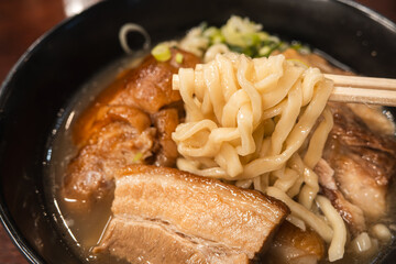 Traditional Okinawa Soba noodle soup with pork belly and ribs in a black bowl.