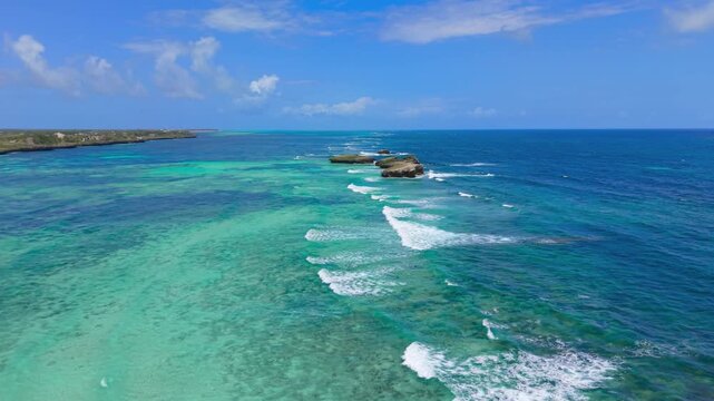 Aerial view of turquoise ocean water and small rock islands along the coastline with white waves breaking under a blue sky at Watamu Beach, Kenya.