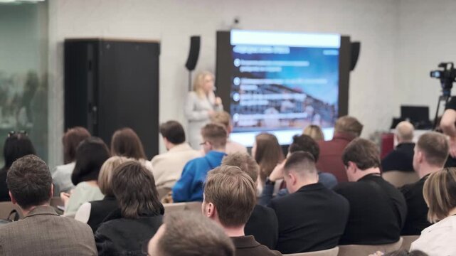 Attentive audience watching business presentation on large screen, modern tech seminar setting, professional networking and learning atmosphere.