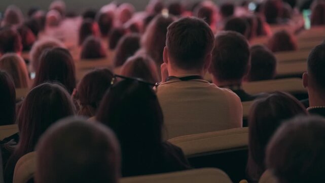 Panoramic view of business conference audience seated in auditorium, rear view of attendees in soft low light, focused atmosphere, networking, learning, professional event energy