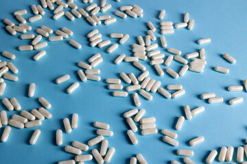 Obraz premium White capsules scattered blue background health supplements pharmacy excess self-medication overuse awareness studio flat lay