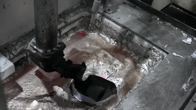 Close-up of a robotic ladle dipping into a pool of molten metal to extract a precise measure for an automated die-casting machine