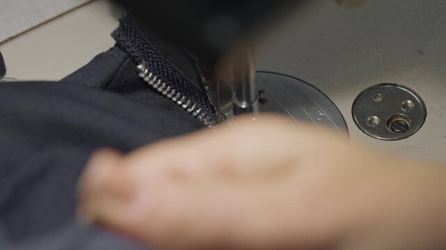 Female ringed hands guide dark denim fabric under presser foot of industrial sewing machine