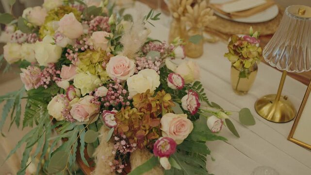 Lush wedding centerpiece with pink roses, ranunculus, hydrangea and eucalyptus on table