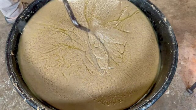 Traditional scrapple being stirred in a large cast iron kettle over heat.