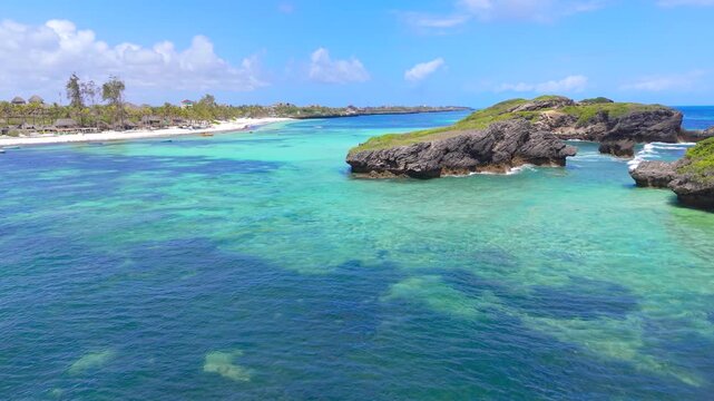 Aerial view of turquoise ocean water, white sand beach, and rocky islands with small boats anchored near the shoreline in Watamu Beach, Kenya.